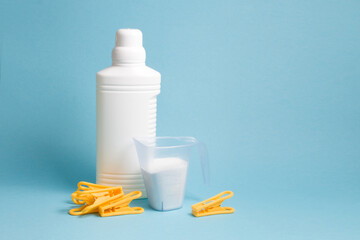 bottle with liquid gel for washing without a label and a measuring cup with washing powder, blue background copy space, washing white linen, a few yellow clothespins on the table