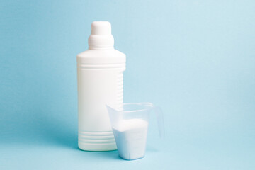 bottle with liquid gel for washing without a label and a measuring cup with washing powder, blue background copy space, washing white linen, bleach in a white bottle