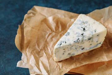 Blue cheese on a parchment paper on dark textured background	