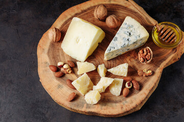 Cheese plate with honey and various nuts on an authentic wooden board. Dark black embossed background. Appetizer, aperitif, snack table.