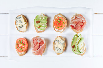 Assorted italian bruschetta. Appetizing mediterranean bruschetta. Variety of small sandwiches. Top view, light wooden background