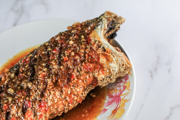 Thai Tradition food Deep fried fish topped with sweet and sour sauce on white plate serve to customer.Selective focus on Mable table.Delicious dish Restaurant Cooking Seafood.