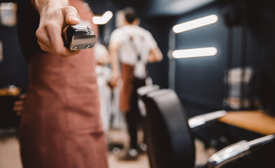 Barber holds hair clipper in modern barbershop for men, brown retro