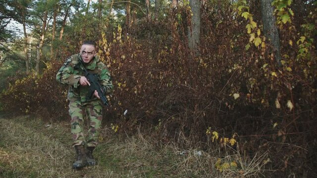 The hunter climbs out of the bushes and aims a gun at an object in the forest