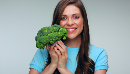 Smiling woman in blue dress holding big green broccoli.