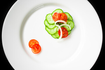 Cucumber and cherry tomato salad with onions on a white plate. Vegetables are cut into slices