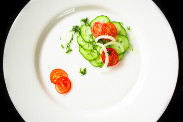 Cherry tomato, cucumber and onion salad on a white round plate. Vegetables are cut into slices