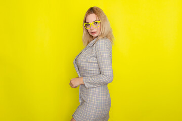 Attractive blonde woman in plaid jacket dress over yellow background
