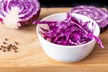 Obraz na płótnie Canvas Some shredded cabbage in a white bowl. The bowl stands on a wooden Board, with black pepper peas and cabbage in the background