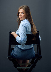 woman with long hair  sitting back on movies director chair turns to  side.