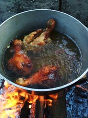 Three crispy, juicy chicken legs are frying  in boiling oil in a cauldron on an open fire