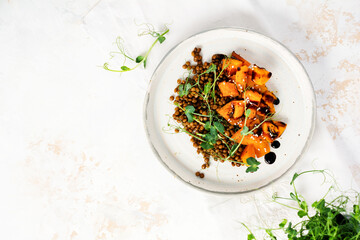 Salad with baked pumpkin, lentils and balsamic dressing garnished with peas microgreens on a light background. Healthy vegan food, top view.