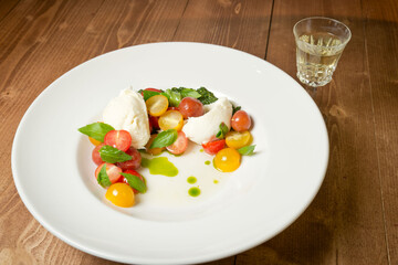 Caprese salad in unusual serving with pesto sauce. On a white plate. On a rustic wooden background