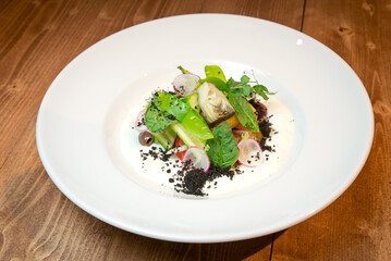 Warm vegetable salad with artichokes, peach and truffle. On a white plate. On a rustic background