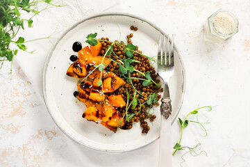 Salad with baked pumpkin, lentils and balsamic dressing garnished with peas microgreens on a light background. Healthy vegan food, top view.