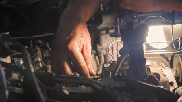 Close-up front view of a mechanic with dirty hands repairing the engine with lamp. 4K (UHD)