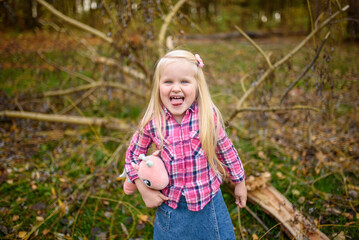 Little blonde girl in a shirt and denim shorts walks in the autumn park. Girl shows tongue. close-up.