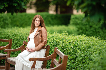 Beautiful pregnant woman sitting in the park on the bench.