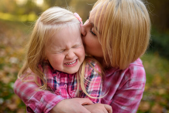 Mom and daughter in pink shirts. A woman kisses a girl. The girl is crooked. Close-up.