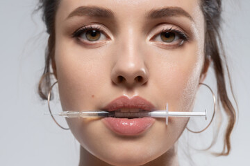 Young beautiful woman face with syringe in mouth portrait. 