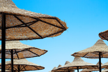 Straw umbrellas on the beach on the blue sky background
