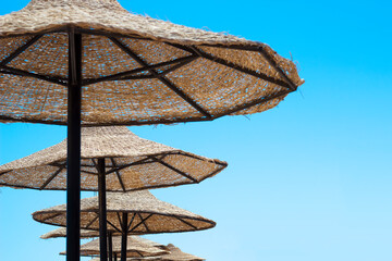 Straw umbrellas on the beach on the blue sky background
