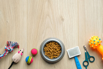 Fototapeta na wymiar Pet care and training concept. Bowl with dry kibble food and accessories for dog and cat on wooden table. Flat lay, top view. Veterinary shop banner mockup.