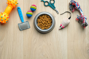 Flat lay composition with bowl with food for cat or dog and accessories on wooden background. Pet care and training concept.