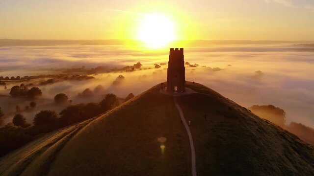 Orbiting the golden sunrise behind Glastonbury Tor and the surrounding misty fields in Somerset.