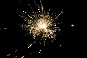 Yellow sparkler countdown on fire with spread of glitter sparks. Luxury entertainment at e.g. New Years Eve, Independence Day or birthday party celebration. Glowing light spark on dark background