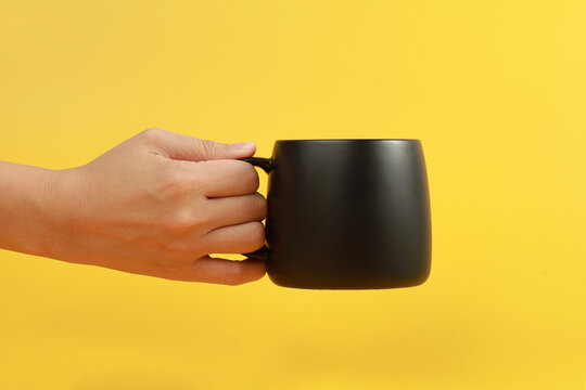 Female hand holding a coffee mug isolated on yellow background