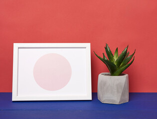 white photo frame and ceramic pot with a growing plant on a blue wooden table