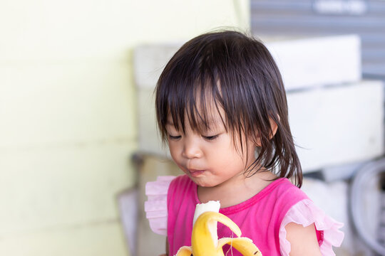 Portrait image of baby 1-2 years old. Happy Asian child girl enjoy eating a banana with sweet smiling. Food and healthy kids concept.