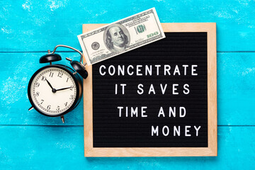 Inspirational motivational business quote Concentrate. It Saves Time and Money words on blue letter board with hundred dollar bill on wooden background near vintage alarm clock. Motivation concept.