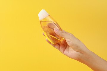 Female hand holding a bottle of hand sanitizer gel over yellow background. Personal hygiene concept.