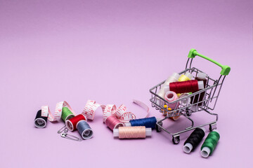 Spools of thread, pins, tape measure and shopping basket with sewing threads on a purple paper background