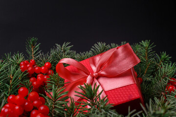 New Year Christmas Xmas holiday celebration red present gift box with satin pink bow, immersed in the needles of a Christmas tree decorated with red berries. Dark festive composition.