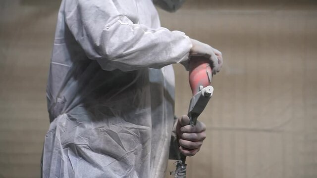 Powder coating of metal products. A man in a White protective and respirator suit pours grey powder into a spray gun in the paint chamber