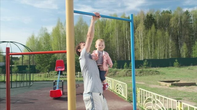 Family work out. Young man does pull ups with his baby. Adult male performs work out with his little child as additional weight.