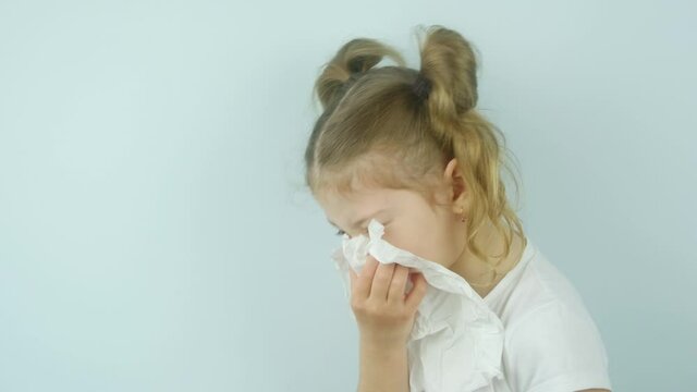 Close-up portrait of a little European girl of preschool age with light hair sneezing and blowing her nose covering nose with white handkerchief. 4k