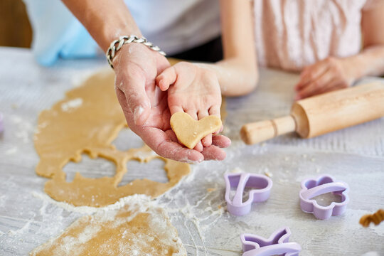 Hands father and his little daughter holding unprepared heart-shaped cookie together, top view.