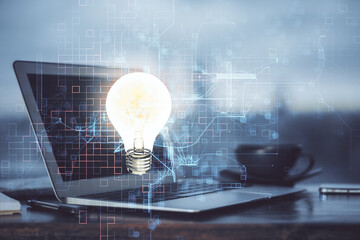 Computer on desktop in office with bulb icon hologram. Multi exposure. Concept of idea.