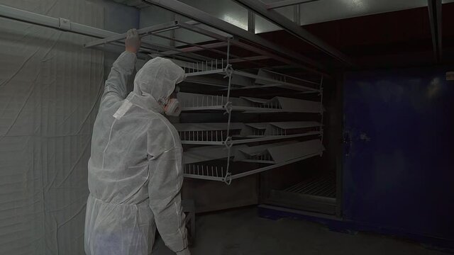 Powder coating of metal products. A man in a White protective suit and a respirator moves metal products into the polymerization furnace