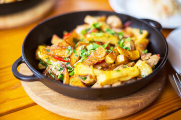 Authentic fried potatoes with bacon and parsley on black pan. Morning atmospheric lighting, fashionable trendy spot soft focus. Preparation for design creative menu.