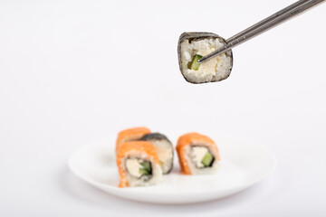 Roll of sushi on chopsticks with sushi roll on white plate on white background