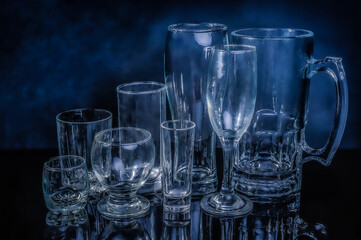 glass drinkwares and stemwares of different shapes and sizes stand side by side on an isolated black background with reflection