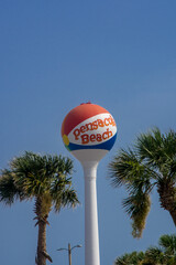 Iconic Pensacola Beach beachball water tower standing above palm trees with a blue sky behind it