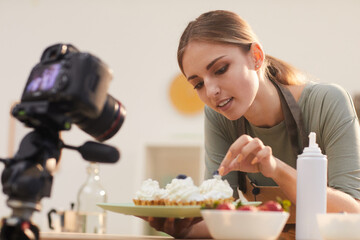 Obraz na płótnie Canvas Young blogger showing the process of decorating the baked cakes and shooting it on the video