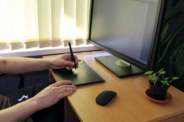 Hands do the work on a graphics tablet in front of the monitor. Close-up plot, side view