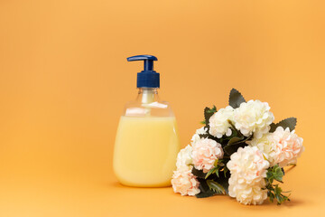 Yellow liquid soap bottle and beautiful delicate flowers on a beige background. Clean hands concept. Shampoo, Liquid Soap, Aromatic Bath Salt And Other Toiletry.